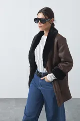 Tapado de efecto cuero negro con interior y detalles de cuello y puños en pelo sintético. Presenta un diseño envolvente con cierre frontal de botones y bolsillos laterales.