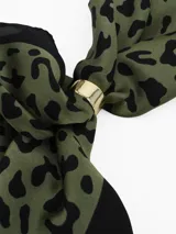 Pañuelo de seda con estampado geométrico en blanco, negro y gris, que incluye un anillo metálico dorado para sujetarlo.