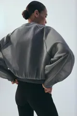 Chaqueta estilo bomber de punto color beige con acabado brillante, cuello redondo, manga larga con puños elásticos y cierre frontal con cremallera.