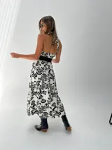 Vestido midi blanco con estampado floral negro, escote halter y cinturón ancho negro.