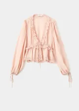 Blusa de viscosa color rosado con escote en V, mangas largas abullonadas con puños ajustables mediante lazos y detalles de puntilla en el escote, bajo y mangas. Presenta un cierre frontal con lazo.