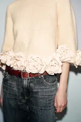 Jersey de punto color crema con cuello redondo y mangas tres cuartos. Presenta un diseño holgado con el ruedo decorado con aplicaciones de flores de tela en relieve.