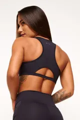 Top deportivo de espalda nadadora con diseño ergonómico, color marrón. Cuenta con un bolsillo integrado en la parte superior de la espalda y una abertura inferior, confeccionado en tejido técnico de alta compresión con detalles reflectivos.