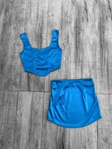 Conjunto de dos piezas confeccionado en tela satinada color azul vibrante. Incluye un top tipo corset con escote cuadrado y una minifalda ajustada de tiro alto.