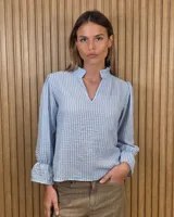 Blusa celeste y blanca a rayas con textura arrugada, escote en V con cuello alto gorguera, mangas largas abullonadas y puños con volados.
