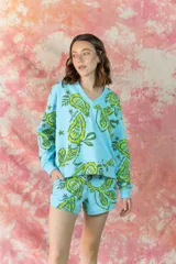 Buzo de cuello en V, manga larga con puños elásticos y diseño holgado. Presenta un estampado botánico en tonos verde lima sobre fondo celeste.