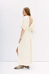 Vestido largo color crema, con escote en V en el frente y espalda. Presenta mangas cortas amplias, talle ajustado con lazo trenzado y tajos laterales.