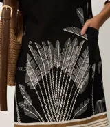Vestido corto de viscosa y lino color negro con escote en V y mangas cortas. Presenta un estampado de follaje en la parte inferior y detalles de franjas horizontales en el dobladillo.