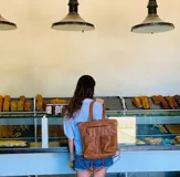 Mochila de cuero marrón con cierre superior y múltiples bolsillos externos. Se puede convertir en bolso de mano o bandolera gracias a sus correas ajustables y extraíbles.