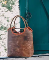 Bolso tipo matera de cuero con textura de reptil, color tostado, con manijas trenzadas y detalles de costura artesanal en los bordes.