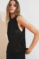 Top negro de tejido de punto abierto con calados en forma de rombos, cuello barco y sisa. Presenta apliques de abalorios a tono.