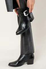 Bota corta de cuero color chocolate, con taco cuadrado y hebilla metálica decorativa en el lateral. Presenta un diseño clásico con punta redondeada.