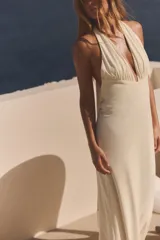 Vestido largo color blanco con cuello halter y escote en pico pronunciado. Detalle de frunces, forro interior y abertura en la espalda.