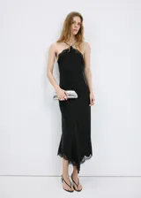 Vestido largo lencero de satén negro, con cuello halter, tirantes finos, detalles de encaje en el escote y en el bajo asimétrico.