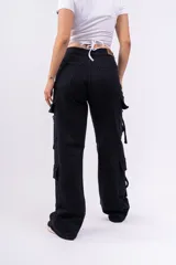 Pantalón cargo negro de jeans sin lycra, corte holgado y tiro alto. Cuenta con múltiples bolsillos laterales con solapa y cordones ajustables.