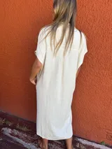 Vestido camisero color crudo, de corte recto y largo midi. Tiene cuello camisero, mangas cortas y cierre frontal con botones.