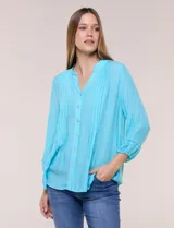 Blusa celeste de silueta suelta y textura liviana, con escote en V, cuello mao y cierre frontal de botones. Cuenta con alforzas verticales en el pecho y mangas tres cuartos con puños elastizados y detalle de galón calado.