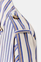 Camisa de manga larga con cuello subido y trabillas en los hombros. Presenta un diseño de rayas verticales en tonos azul, beige y marrón, con cierre frontal de botones.
