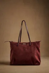 Bolso tipo tote de gran tamaño en color bordó, confeccionado en material sintético con textura de gamuza. Cuenta con cierre superior, correas largas de hombro en tono marrón oscuro y una placa metálica decorativa en el frente.