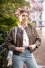 Chaqueta marrón oliva de cuero sintético, corte recto, cuello redondo y cierre frontal con cremallera. Tiene bolsillos con solapa en el pecho y mangas largas con puños abullonados.