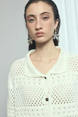 Cardigan de punto calado color marfil, con cuello solapa, cierre frontal de botones oscuros y bolsillos frontales.