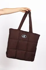Bolso tote marrón con diseño acolchado a cuadros y logo ovalado con letras en el centro.