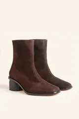 Bota de caña media confeccionada en cuero vacuno negro, con diseño minimalista y cierre trasero. Presenta un taco cilíndrico de madera tallada y punta cuadrada.