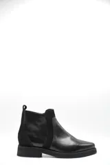 Bota corta tipo chelsea de cuero negro, con paneles laterales de gamuza y suela plana de goma. Presenta un diseño minimalista con tirador en la parte trasera.