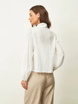 Blusa de textura arrugada con cuello alto y lazo frontal para anudar. Presenta mangas largas con puños elásticos y corte recto.