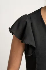 Blusa negra de manga corta con volados en los hombros, escote en V y cierre frontal con botones pequeños.
