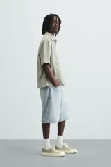 Bermuda de denim de algodón, color azul medio lavado, de corte ancho (baggy fit) y largo hasta la rodilla. Presenta cinco bolsillos y cierre frontal con cremallera y botón.