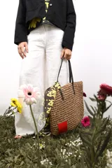 Bolso de rafia color beige con asas de cuero marrón y parche rojo en una esquina.