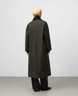 Abrigo largo de color verde militar con corte recto y tejido de efecto encerado. Posee cuello italiano de pana en contraste, cierre frontal oculto por solapa y bolsillos laterales inclinados.