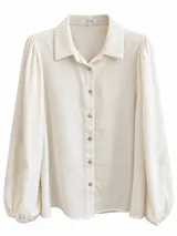 Camisa de manga larga color beige con cuello camisero, cierre frontal de botones y detalles bordados en las mangas abullonadas.