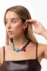 Collar de diseño irregular compuesto por una mitad de cuentas de piedra turquesa y la otra mitad de cuentas de madera, piedras naturales y acrílico, con un dije central en forma de gota roja.