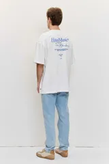Remera blanca de manga corta, corte oversize, con estampa en la espalda de una flor sobre fondo difuminado verde y blanco.