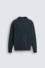 Jersey de punto grueso con estructura de volumen, corte relajado, cuello redondo y manga larga con puños y ruedo acanalados. Presenta un diseño bicolor con trama en tonos verde oscuro y azul.