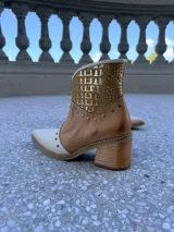 Bota tejana de cuero combinado en napa y croco, con puntera y caña en tonos beige y tostado, y detalle metalizado dorado. Presenta tachas decorativas en la puntera y el empeine, y cuenta con taco de madera de 6,5 cm.