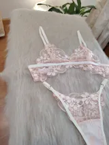 Conjunto de lencería compuesto por un bralette triangular y una bombacha tipo tanga, confeccionados en encaje floral color coral con detalles de elásticos en tono champagne.
