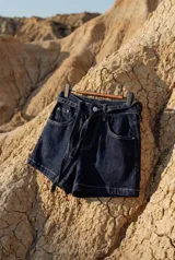 Short de denim elastizado en color azul marino, con tiro alto y lazo ajustable en la cintura. Presenta pespuntes en contraste, bolsillos frontales y cierre frontal con botón y cremallera.