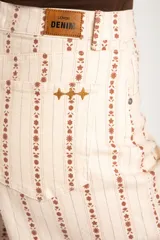 Pantalón jean wide leg de tiro alto, color beige con estampado vertical de líneas y flores marrones, de corte holgado y diseño de cinco bolsillos.