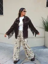 Chaqueta de gamuza color chocolate, con diseño de flecos en el frente y la espalda, decorada con tachas metálicas en cuello, hombros y puños. Cuenta con cierre frontal de botones y forro interior.