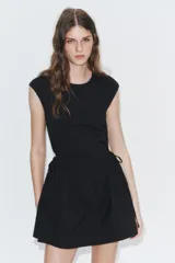 Vestido corto negro confeccionado en 100% algodón, de cuello redondo y mangas cortas. Presenta detalle de lazadas en los laterales de la cintura y falda con vuelo.
