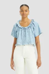 Camisa celeste con bordado de flores blancas, escote con volados y lazo ajustable, manga corta y cierre frontal con botones.