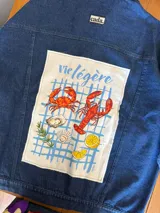 Campera de jean azul oscuro, de corte oversize, con cuello clásico, cierre frontal con botones metálicos, bolsillos con solapa en el pecho y estampado de lunares grandes en blanco y negro en la espalda.