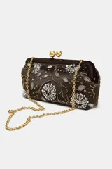 Bolso tipo clutch de efecto terciopelo color marrón, con bordados florales, apliques de brillos y lentejuelas. Cuenta con cierre de clip metálico dorado y cadena metálica extraíble.