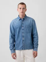 Camisa de jean de corte recto y calce relajado, con cierre frontal de botones metálicos, cuello clásico y un bolsillo frontal en el pecho.