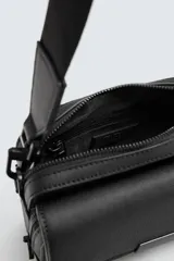 Bandolera negra con textura grabada, compartimento principal con cierre de cremallera y bolsillo interior con cremallera. Bolsillo frontal con solapa y cremallera. Asa de hombro removible y ajustable.