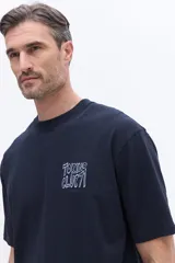 Remera de manga corta color azul marino con cuello redondo y calce regular. Presenta un estampado artístico en la espalda con diseño floral estilizado y tipografía.