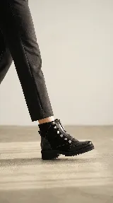 Bota corta de cuero negro con diseño versátil que incluye una pieza frontal removible con cierre y detalles de tachas metálicas. Presenta una combinación de texturas en cuero liso y cuero con textura tipo reptil en el talón, con suela track de goma.